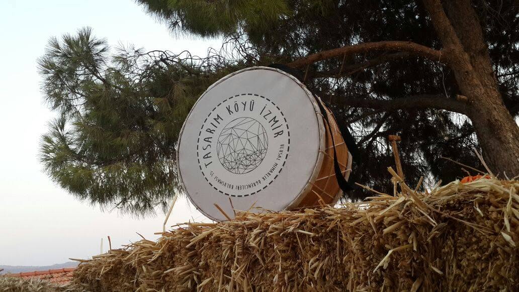 A davul (drum) branded with the Tasarım Köyü İzmir logo, resting on a hay bale at the workshop site