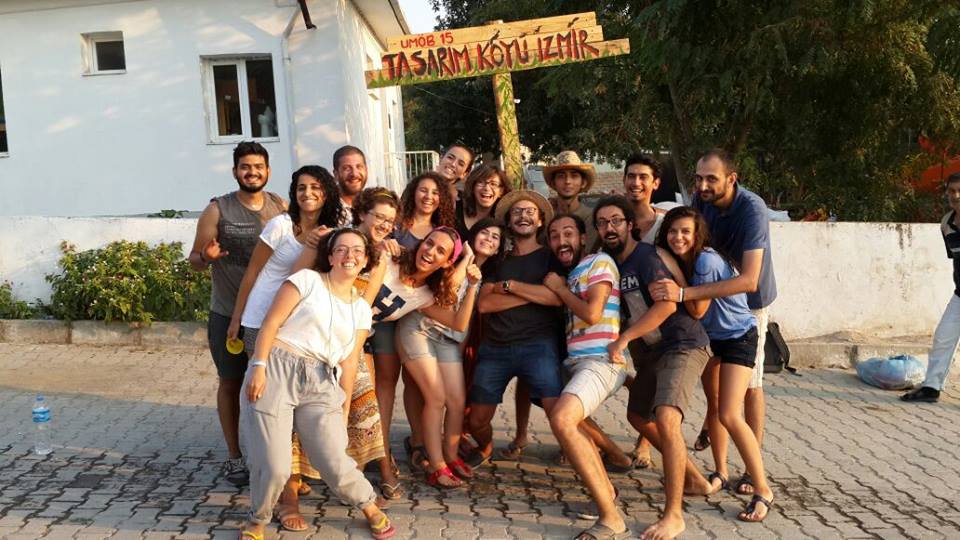 Group photo in front of the hand-built wooden ÜMOB 15 / Tasarım Köyü İzmir entrance sign