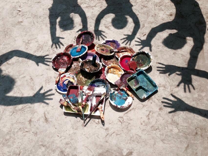 A second overhead shot of the paint palettes, brushes, and children's shadows reaching in from around the circle