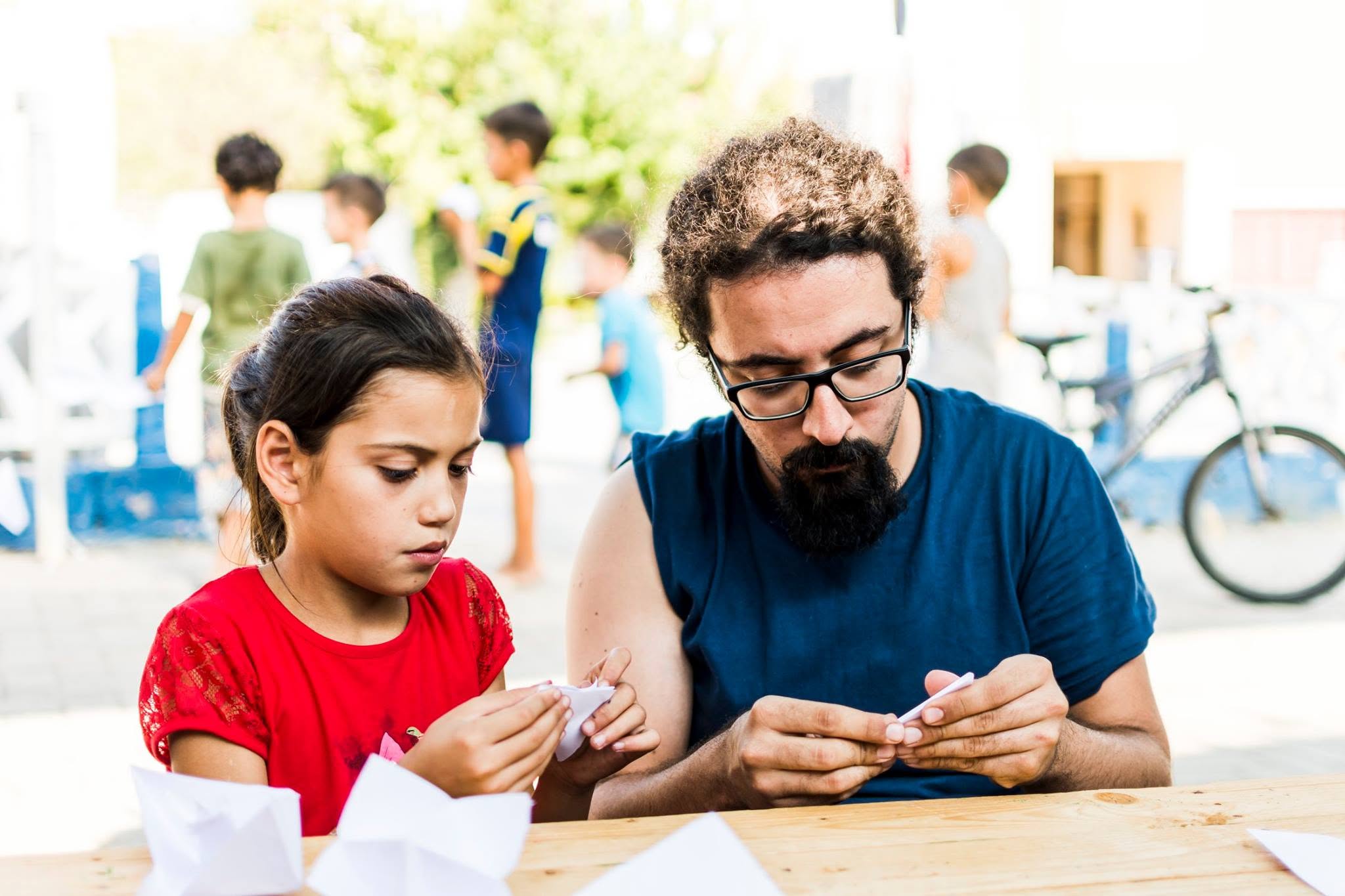 An organizer and a child folding paper together at a community workshop table