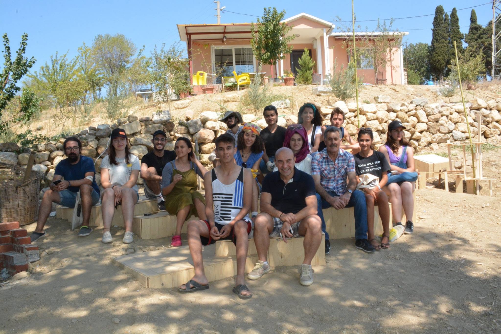 The full Tasarım Köyü İzmir 2016 group seated on wooden steps outside the workshop house at Turgutköyü
