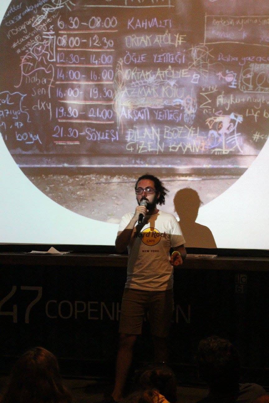 Presenter with microphone in front of a screen showing the same daily schedule, chalked onto a blackboard