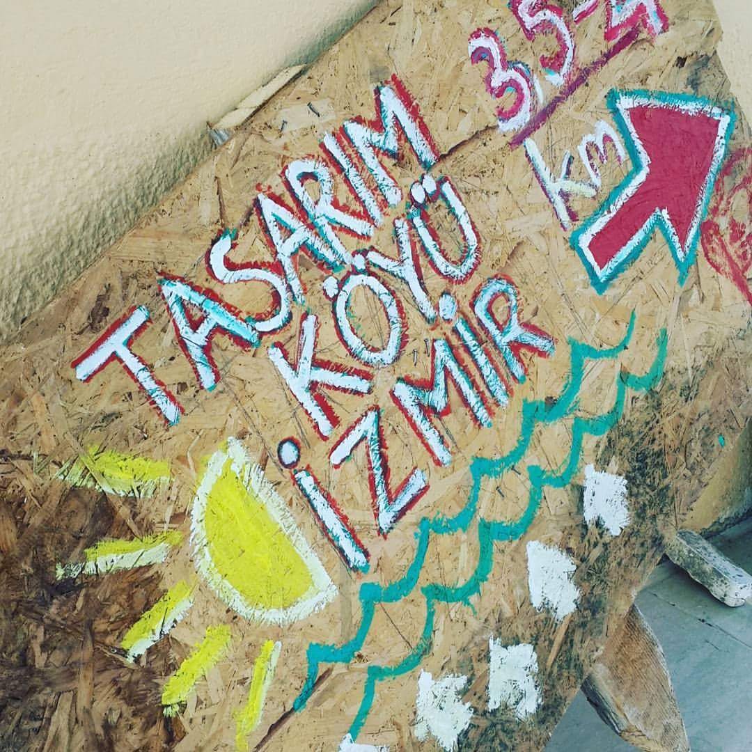 Hand-painted plywood sign reading Tasarım Köyü İzmir, 3.5 km
